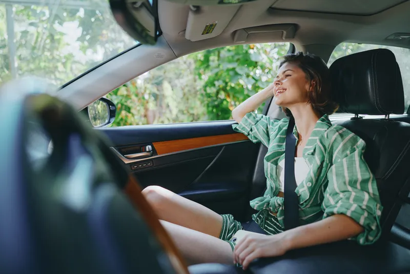 Young woman sits in a car, wearing a seatbelt, smiling and relaxed as sunlight pours through the window.