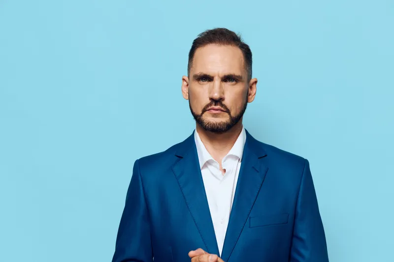 A focused business professional stands against a solid blue backdrop, conveying confidence, calm leadership, and decisive mindset in a corporate setting.