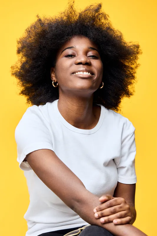 Smiling female model with natural textured hair against a vibrant yellow background, showcasing joy and confidence in casual attire