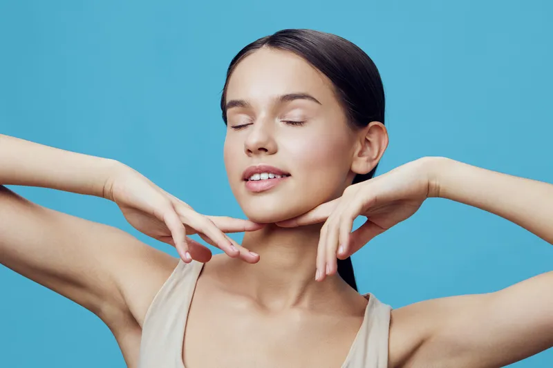 Beautiful young woman with closed eyes enjoying self care against a vibrant blue background, exuding confidence and tranquility in a light tank top