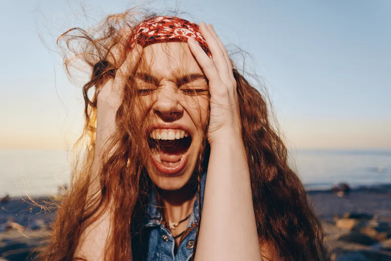 Lifestyle woman with modern boho-western denim street style laughing loudly with eyes closed, vibrant film color tones enhancing energetic outdoor expression.