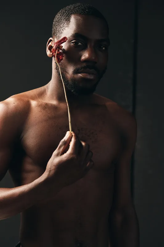 Creative conceptual portrait of African man with dark skin holding dried flower near face in studio. Artistic visual style with bare torso and moody lighting for emotional expression.