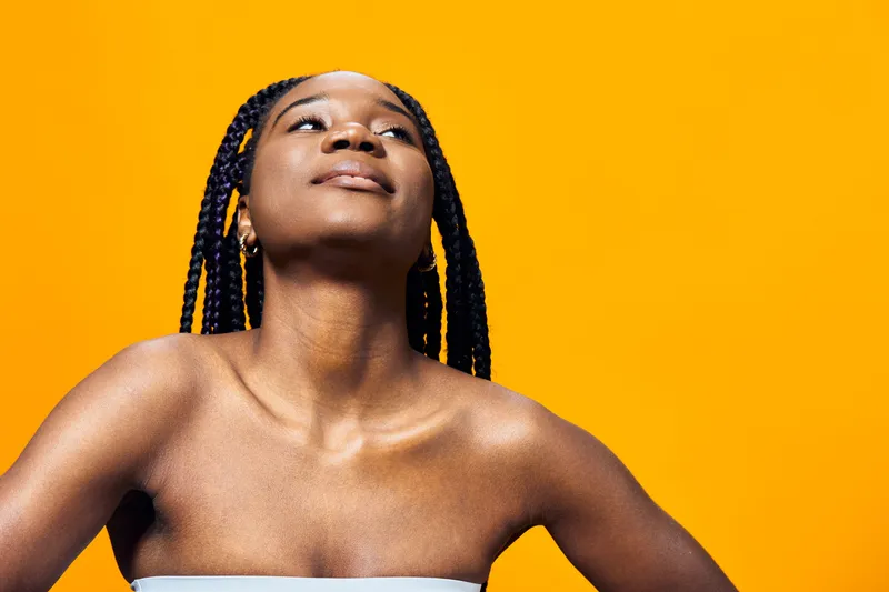 Confident young woman with braided hair, posing against a vibrant yellow background, expressing self assurance and empowerment, ideal for wellness and lifestyle themes