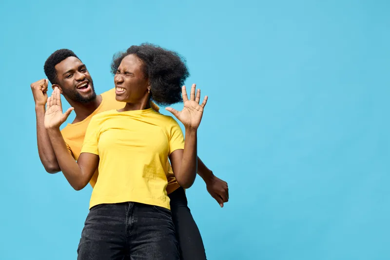 Joyful couple celebrating together in matching yellow outfits against a vibrant blue background, expressing happiness and connection through playful emotions