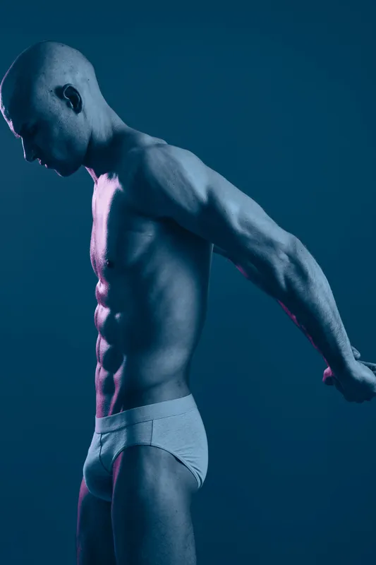 Toned man in a dramatic pose showcasing strength and determination in a blue light, emphasizing muscles and physique. Perfect for fitness and wellness themes.
