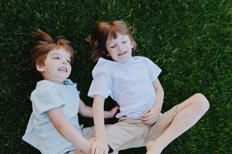 Happy children enjoying a sunny day lying on green grass, laughing and playing together in a cheerful atmosphere, showcasing the joy of childhood and friendship.