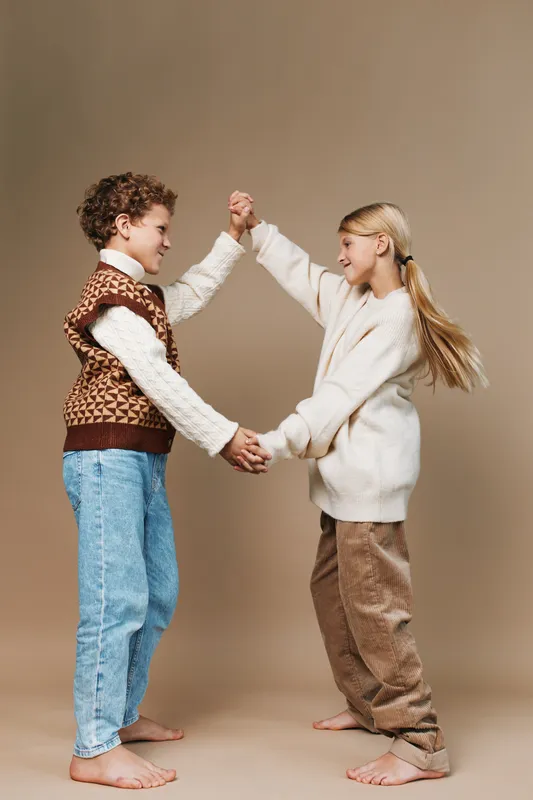 Authentic moment of play and friendship in a school lifestyle scene, featuring two young students dancing hand in hand, expressing curiosity, joy, and genuine connection.