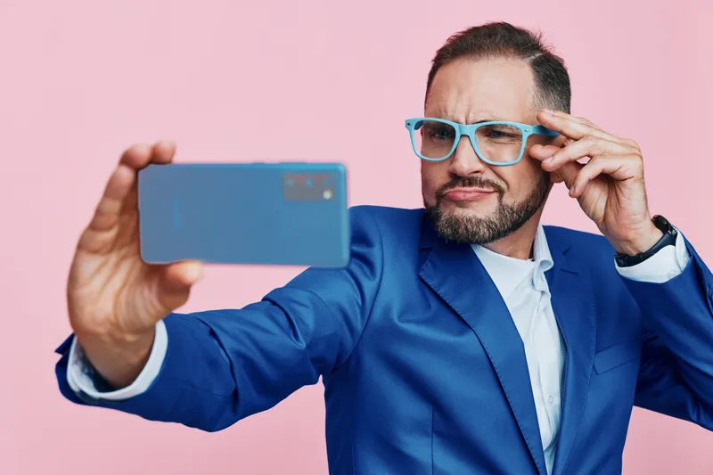 A professional businessman captures a stylish selfie against a vibrant pink backdrop, a colored isolated background that enhances a confident pose and focused expression.