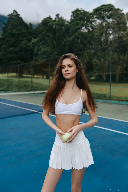 Young athletic woman in white sportswear holding a tennis ball on a blue court, exuding confidence and focus, perfect for sports and fitness themes