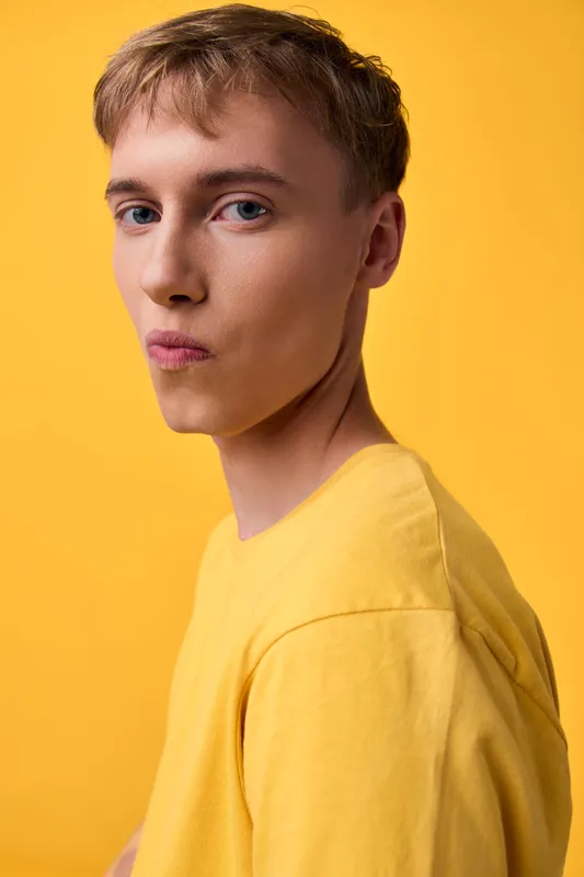 Young male in a yellow tee against a yellow backdrop, close up, soft studio lighting, thoughtful expression, minimal styling, bright fashion mood for lifestyle use