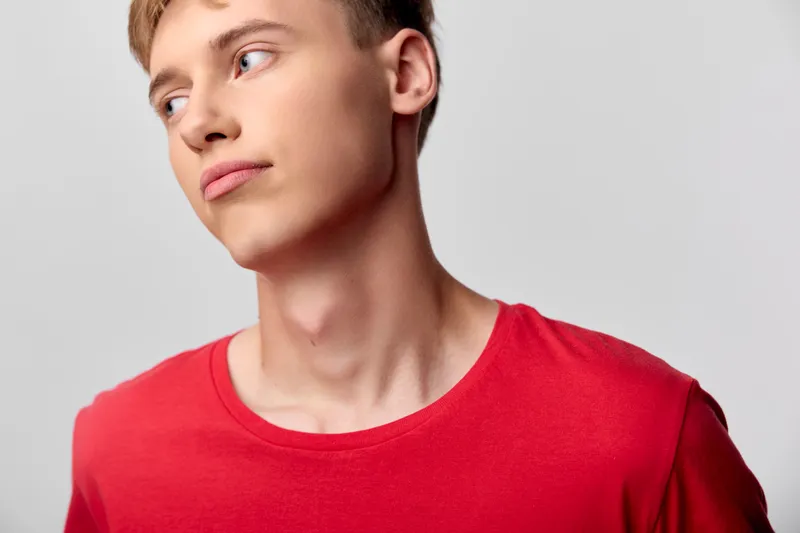 Man, young, side profile with thoughtful expression in a red shirt, casual style, pensive mood, clean studio lighting and minimal background.
