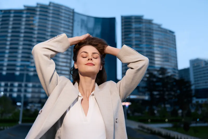 Woman enjoying calm moment outdoors in business casual clothes with modern cityscape background during daytime