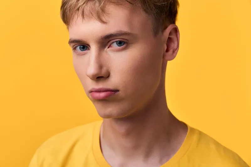 Closeup of a young male in a bright yellow studio backdrop, showcasing a calm expression and contemporary style suitable for fashion, lifestyle or beauty projects with a clean minimal vibe