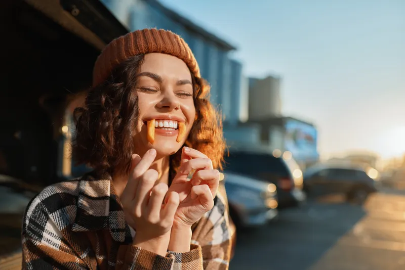 woman smile candid golden fries outdoor beanie laughter street sunlight captured in golden hour glow, playful authenticity and emotional storytelling of youthful mindful living and cozy urban joy