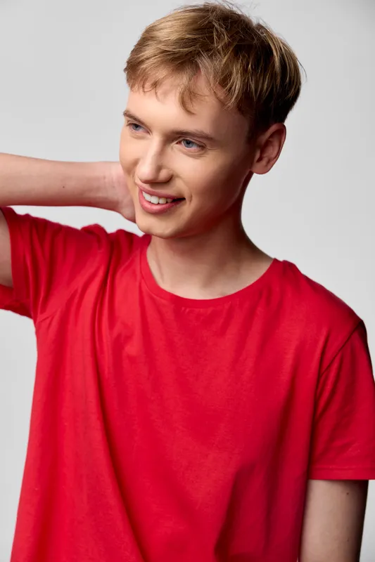 Smiling young man in a red t shirt poses casually with a hand at the neck, conveying relaxed youth fashion, lifestyle and confidence for stock imagery and versatile marketing campaigns