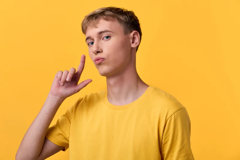Young man in a yellow shirt against a bright yellow backdrop, posing with a thoughtful gesture near his temple, studio style, casual mood, creative concept for lifestyle and fashion visuals