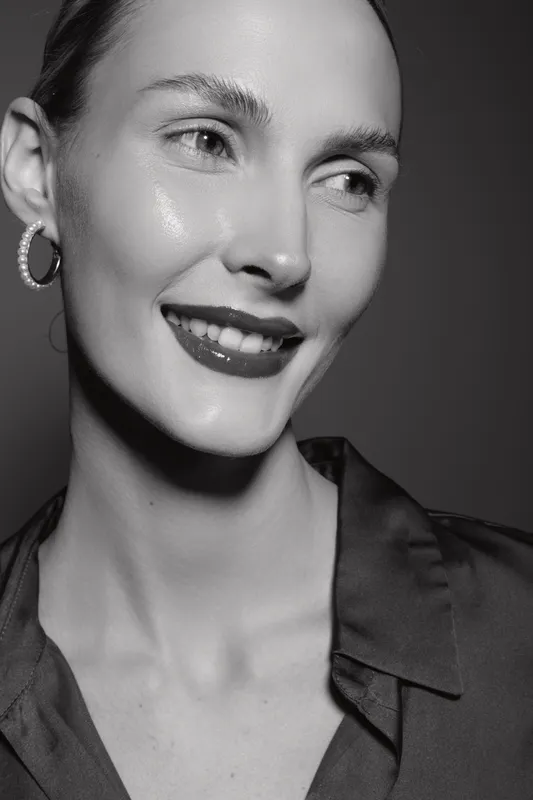 Smiling Caucasian woman with light skin and short hair wears hoop earring and dark shirt. Studio portrait in black and white with soft lighting. Concept of natural beauty and happiness.