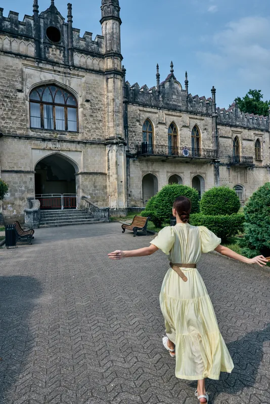 Castle courtyard scene with a woman in a pale yellow dress running toward ancient stone arches inviting sense of adventure and exploration in a historic setting