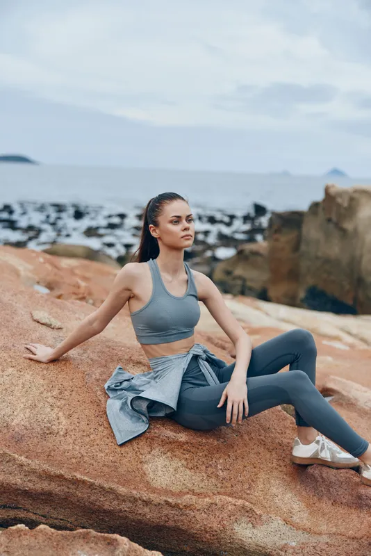Young female model in athletic wear, showcasing confidence and serenity on rocky beach, perfect for healthy lifestyle and fitness promotions