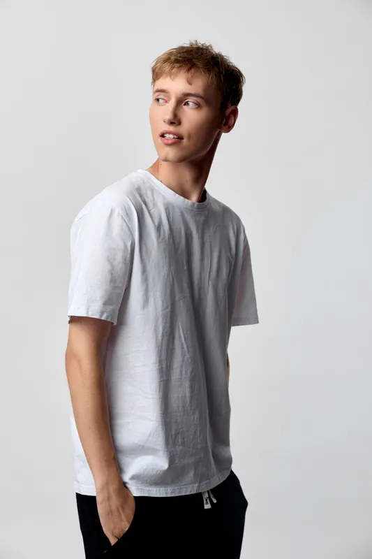 Man in a white t shirt stands at a slight angle with relaxed pose, soft studio lighting, clean background, casual fashion for everyday wear, modern minimal wardrobe.