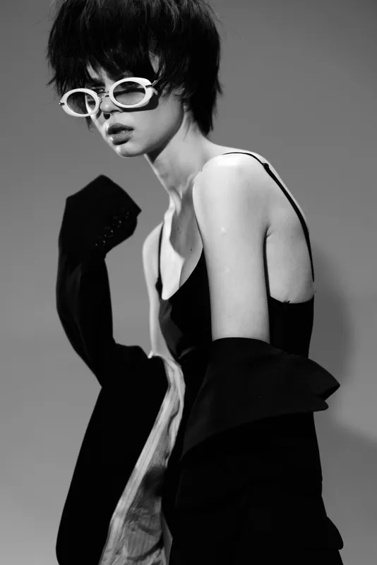 Woman with short hair wearing white sunglasses and black outfit in stylish black and white portrait.