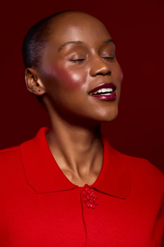 Close-up of a happy dark skinned African woman with closed eyes wearing a red blouse. The studio portrait on red background highlights joyful expression and glossy makeup. Beauty concept.