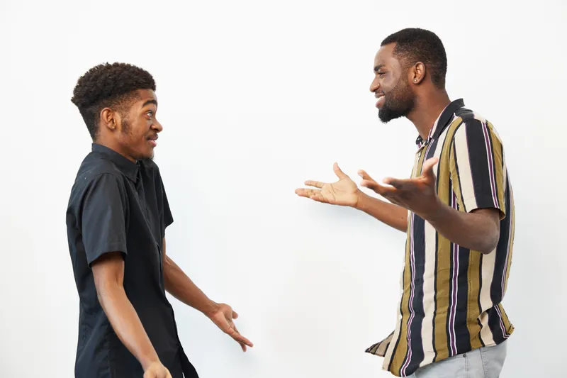 Two black men sharing a joyful conversation, expressing emotions in a relaxed setting, showcasing cultural connection and camaraderie. The atmosphere is lively and engaging.