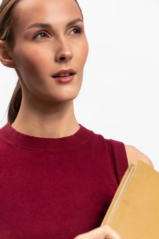 Young woman in red sleeveless top holds a book while looking thoughtfully away. Studio portrait on white background. Concept of education, knowledge, and contemplation.
