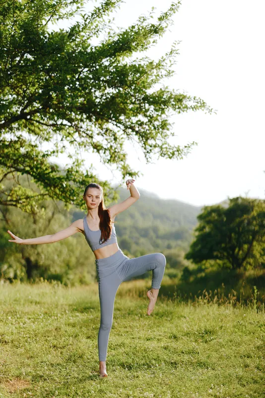 Young athletic woman practicing yoga outdoors in a serene green landscape, embodying tranquility and strength with a smile