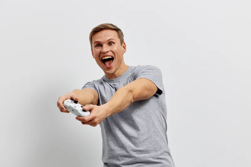 excited young man holding game controller play video games white background casual clothing emotion digital detox concept