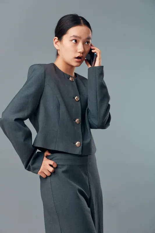 Businesswoman in gray suit talking on smartphone with surprised facial expression against plain background. Professional young woman engaged in communication in formal outfit for work.