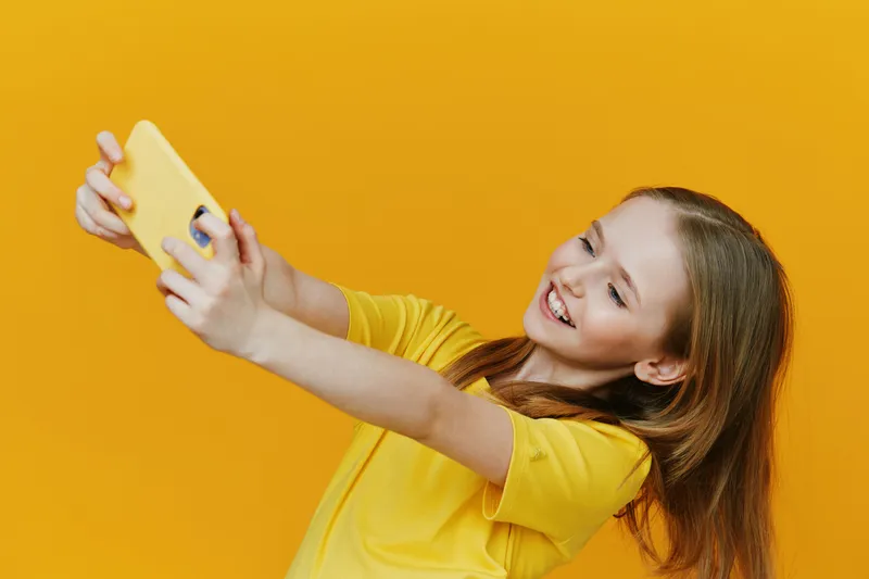 Happy young girl taking a selfie against a bright yellow background, wearing a cheerful yellow t shirt, expressing joy and excitement in a vibrant, playful setting