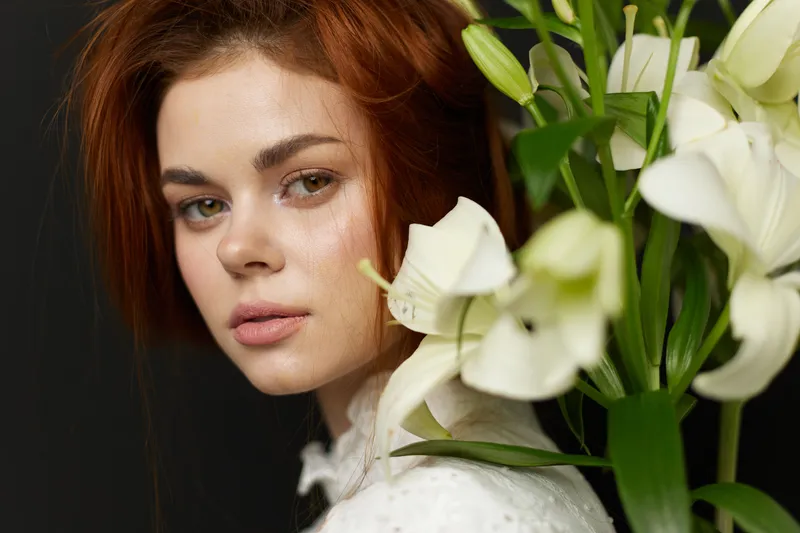 Portrait of a young woman with red hair and fresh white lilies, conveying a sense of tranquility and natural beauty in a minimalistic setting