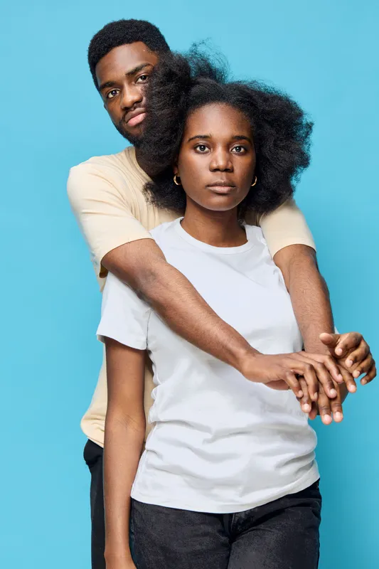 Young African couple embracing against a blue background, expressing love and connection with casual clothing and natural hairstyles, showcasing joy and intimacy