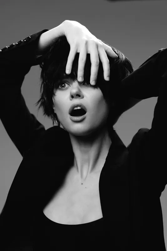 Black and white portrait of expressive woman with short hair in dark clothing showing surprise and emotion.