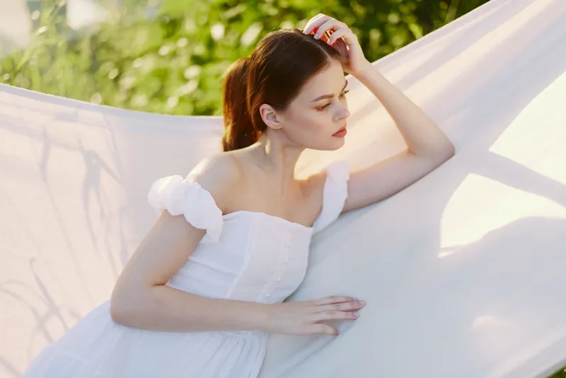 Young woman in a white dress, enjoying a serene moment outdoors, surrounded by lush greenery, evoking feelings of tranquility and joy