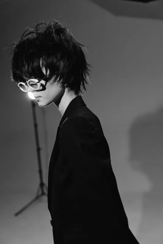 Black and white portrait of a woman with short hair wearing unique eyeglasses in a studio setting.