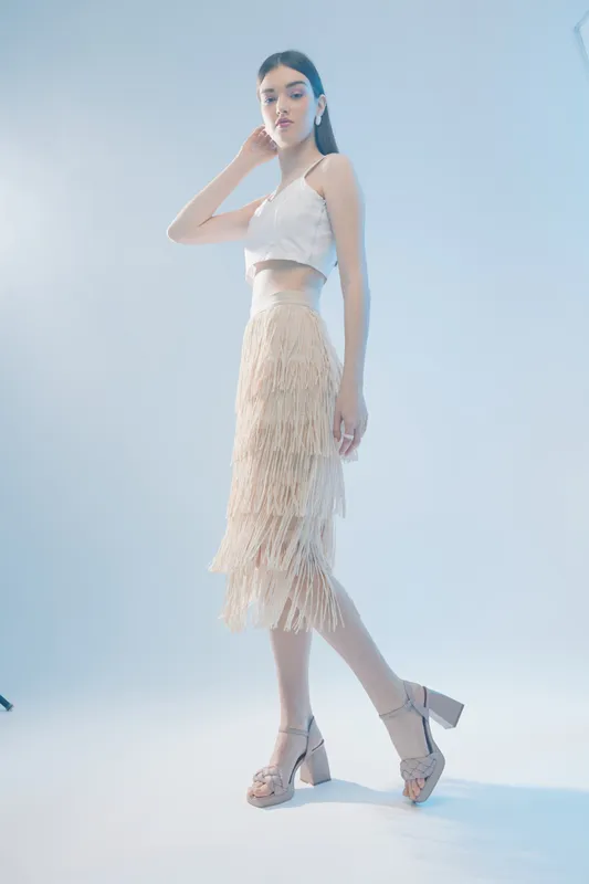 Woman beauty fashion model wearing a white crop top and fringed skirt posing on a light background. Studio shot with soft lighting for style and elegance concept.