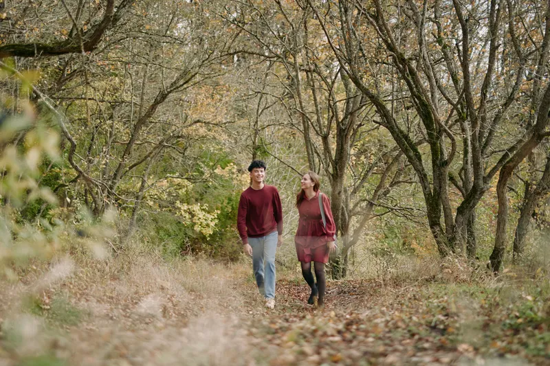 A candid scene emphasizing authenticity and credibility as two walkers share a quiet moment along a sunlit forest path, surrounded by autumn leaves and gentle, natural light.