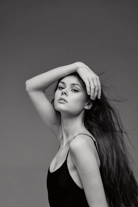 Black and white portrait of a young woman with long hair posing elegantly in a black dress against a plain background.