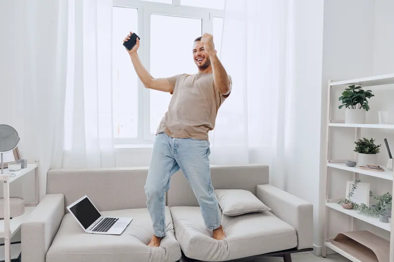 Happy man celebrating while working from home, embracing emotional minimalism and soft masculinity in a bright, modern living space.