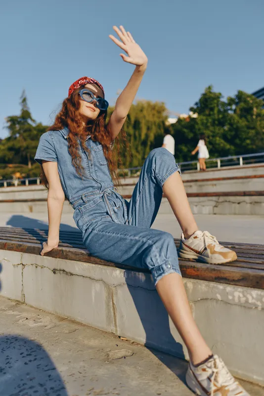 lifestyle woman in modern boho-western denim street style relaxing outdoors in sunny urban setting with film color effect, casual and trendy outfit
