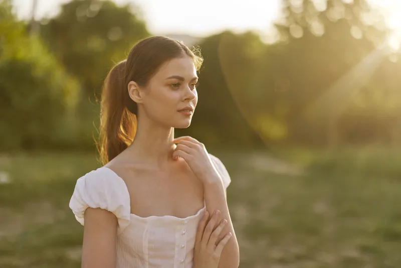 Young woman in elegant white dress enjoying sunset, showcasing serenity and beauty in a natural setting with warm golden tones
