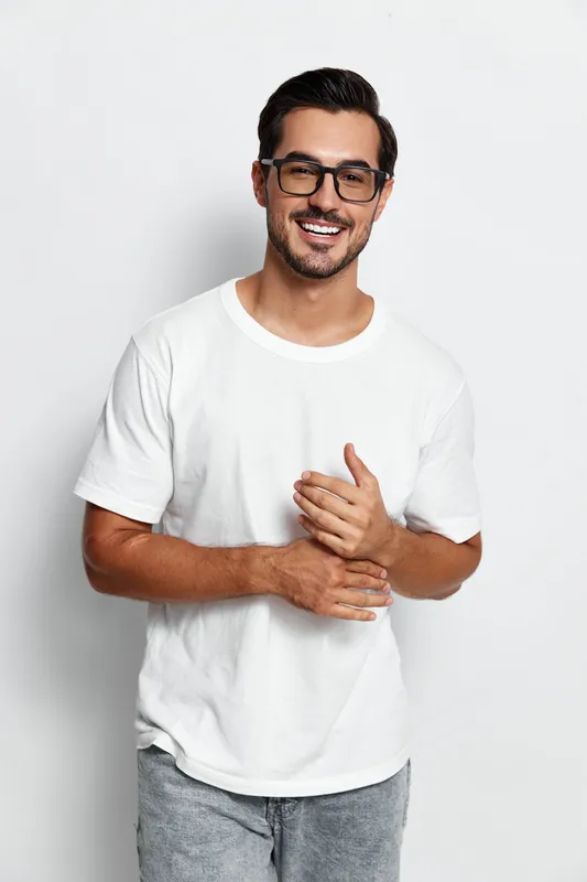 Full body smiling happy cheerful young man wearing white t-shirt stands confidently with hands clasped isolated on plain solid white background. People lifestyle concept.