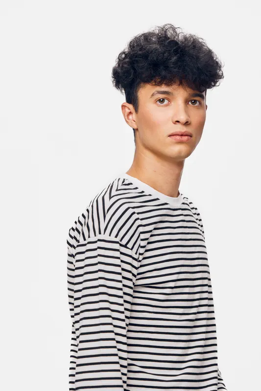 young man with curly hair wearing a striped shirt looking serious against a white background in a studio setting with soft lighting and neutral tones