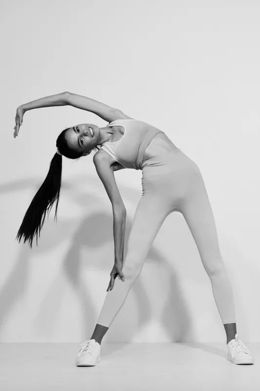 Athletic woman sport fitness stretching in monochrome, wearing leggings and sneakers, showcasing flexibility and strength with long ponytail and focused expression.