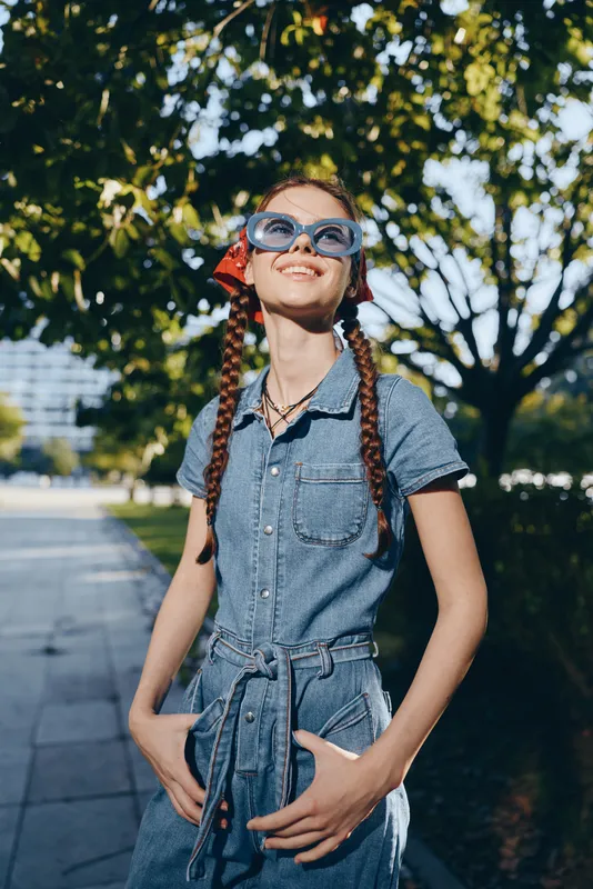 Lifestyle woman in modern boho-western denim street style with sunglasses, smiling and enjoying sunny urban outdoors, film color effect creates warm mood.