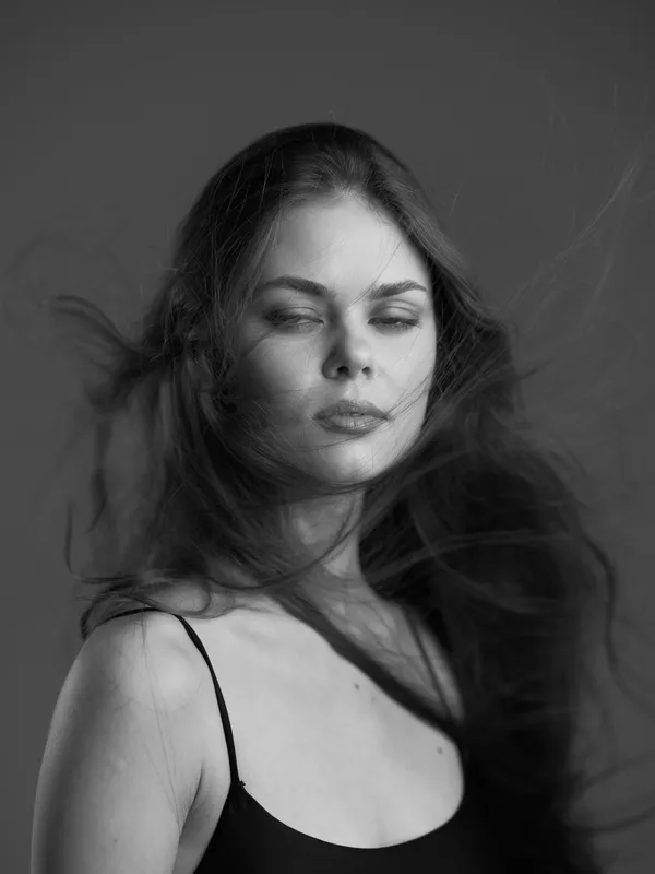 Black and white portrait of a young woman with flowing hair and a serene expression in a studio setting.