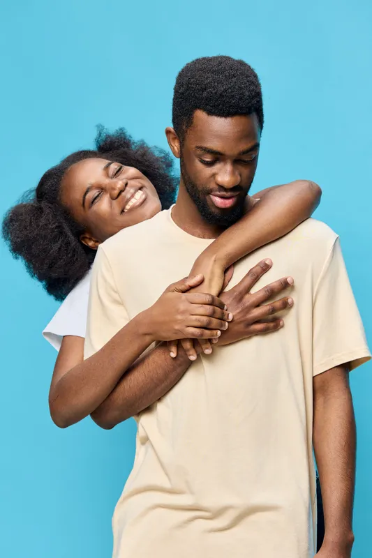 Young African couple embracing against a bright blue background, showcasing joy and affection, wearing casual outfits that reflect a contemporary style