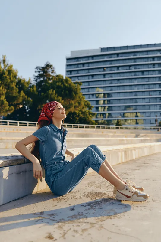 Lifestyle woman in modern boho-western denim street style relaxing outdoors with film color vibrancy under natural sunlight on urban steps during daytime.